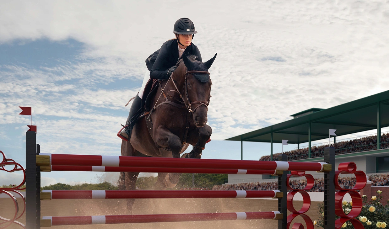 A focused rider, dressed in black, rides a powerful horse and clears a red and white obstacle in a crowded arena on a cloudy day, displaying unwavering determination.